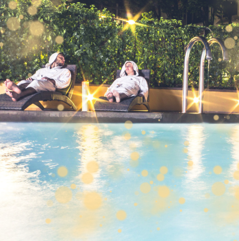 Due persone rilassate a bordo piscina con accappatoi bianchi.